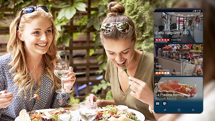 Due donne che mangiano insalate in un ristorante e uno schermo che mostra Bixby che fornisce informazioni sui ristoranti che vendono insalate apprendendo routine.