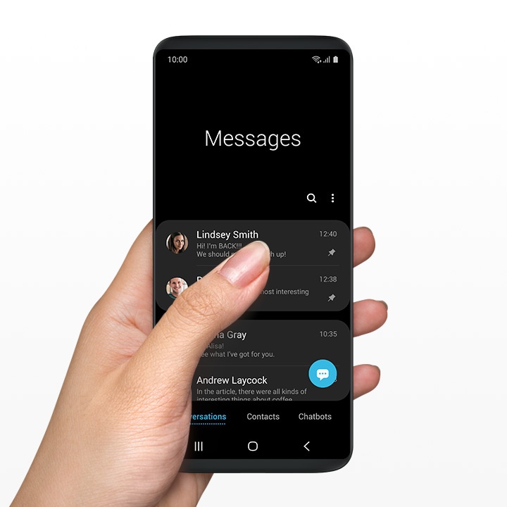 A hand holding a smartphone with One UI Messages application onscreen.
