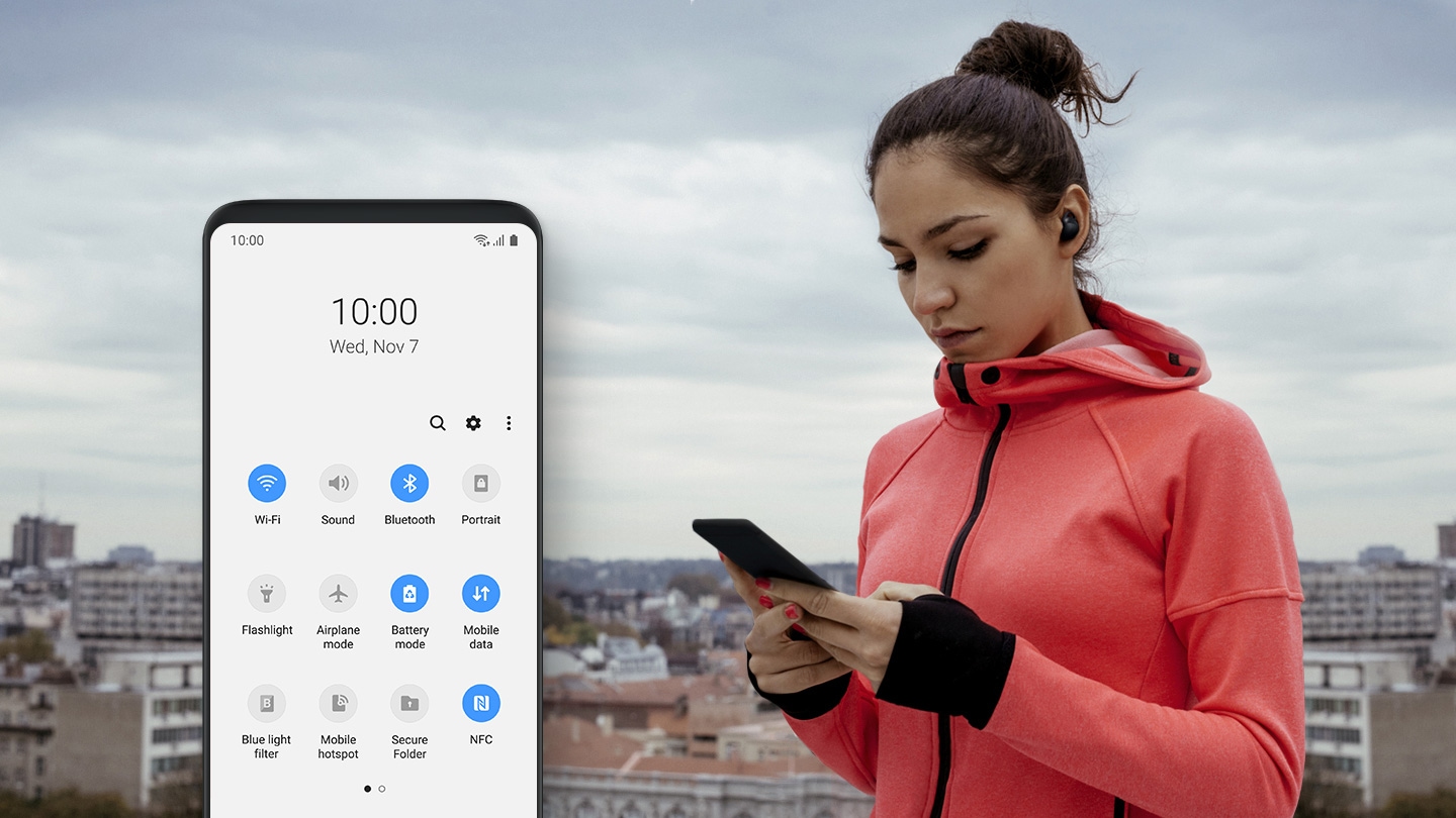Image of woman in workout clothes holding a smartphone with a smartphone in front with One UI Quick Settings function onscreen