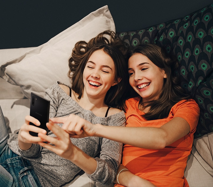 두 여성이 함께 기댄 체 미소를 지으며 스마트폰을 보는 이미지.