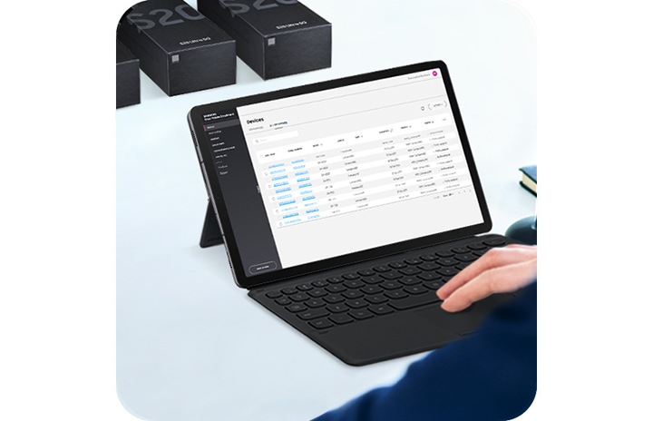 Une personne travaillant sur une Galaxy Tab S6 avec l'interface Knox Mobile Enrollment à l'écran et trois boîtiers Galaxy S20 Ultra à l'arrière.