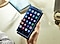 A hand holds up a Galaxy smartphone device with a screen full of various app icons, which are shown on a blue-ish layer floating directly above the screen.