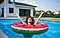 A woman with sunglasses relaxes in her backyard, surrounded by a beach umbrella, inflatable duck and lawn chair.