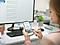 The mother is sitting at her office computer. Using her Samsung Galaxy S9, she is setting the washing cycle on her QuickDrive™ at home, using the Samsung Q-rator app. She smiles at being able to remotely control her washing machine.