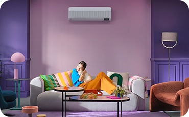 فتاة صغيرة تعانق قطة وهي مسترخية على الأريكة، وخلفها مكيّف الهواء Windfree معلّق على الجدار .