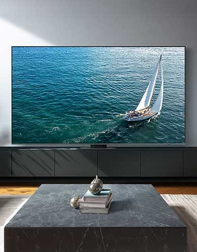 جهاز TV عملاق مقاس 98 بوصة موضوع في منطقة غرفة المعيشة ويظهر على شاشته مركب شراعي.