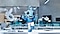 A whimsical looking blue alien dancing happily on top of a lab desk. As if making air quotes, the alien is holding up both hands in a way that mimics the antennae.