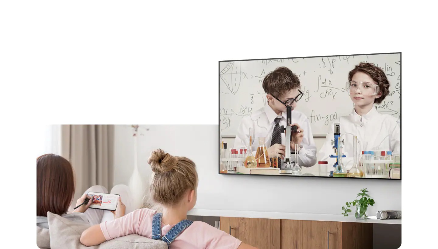 Une fille et sa mère sont assises sur un canapé devant le téléviseur. La fille regarde une série éducative sur le téléviseur pendant que sa mère fait autre chose sur son Galaxy.