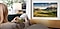 A woman looks at an outdoor mountain scene on her smartphone. The same scene is mirrored onto the screen of a Samsung Smart TV installed on the wall.