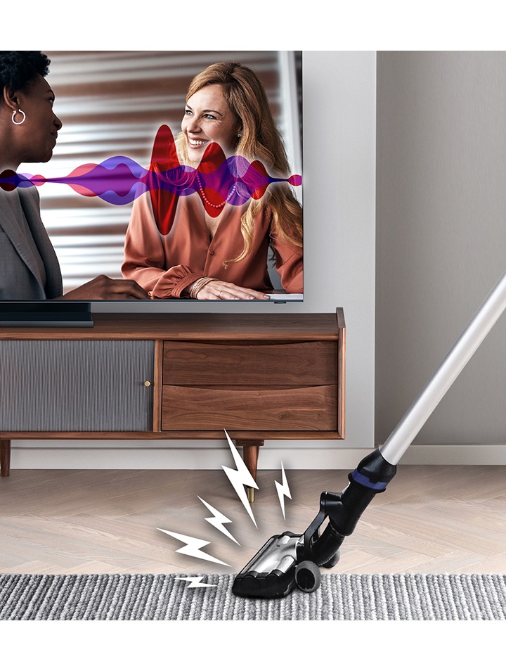 La technologie d’amplificateur voix actif du téléviseur QLED augmente le volume des dialogues sur le téléviseur lorsqu’il détecte des bruits forts. Une image simulée de deux femmes en train de discuter sur un téléviseur QLED, illustrée par un graphique à ondes sonores. Devant le téléviseur, on peut voir un aspirateur. Le bruit de l’aspirateur est illustré par des graphiques d’effets sonores provenant de la tête de l’aspirateur.