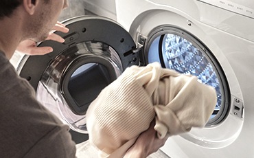 Një burrë është duke futur rrobat në makinën larëse të bardhë Samsung.