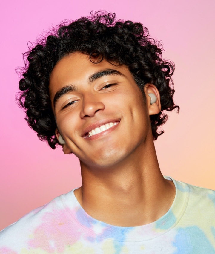 Un joven con cabello negro rizado sonríe con los auriculares Galaxy Buds2 en Blanco en sus oídos.