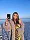 Una mujer con un vestido dorado y un abrigo de piel se toma una selfie en la playa.