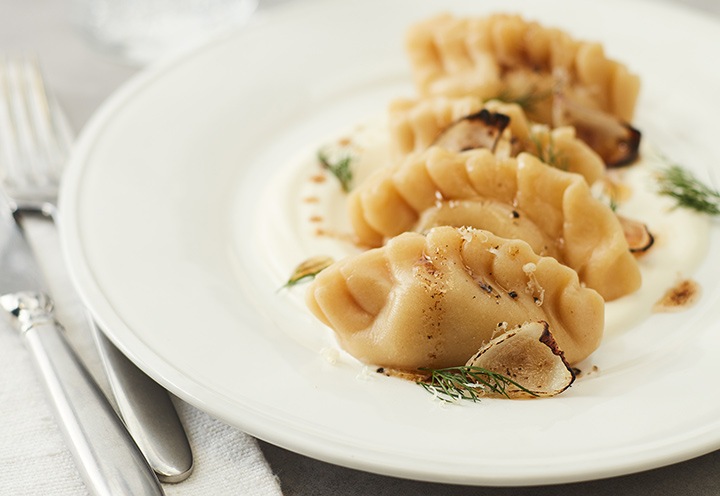 Dumplings al vapor rociados con manteca y condimentados con pimienta negra y ciboulette en un plato blanco.