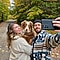 Un hombre con barba que usa un colorido abrigo azul toma una selfie familiar con el Galaxy S21 Ultra 5G. La selfie también muestra a su perro marrón y a una joven mujer con un suéter blanco tejido en una tranquila carretera forestal bordeada por el hermoso follaje otoñal.