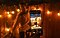 Un hombre parado sobre un pie mientras sostiene el otro pie con la mano. Está frente a una cerca de madera bordeada con una cuerda de luces encendidas. La escena está capturada de noche con un Galaxy S21+, que está en primer plano con temporizador de cinco segundos. El pulgar de una mujer está en el botón del obturador.