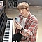 Suga de BTS sentado frente a un piano, sostiene el Galaxy S20 y sonríe porque está hablando con alguien por videollamada