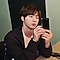 Jin de BTS sentado en un vestidor, tiene los codos sobre el tocador y está jugando con el Galaxy S20