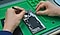 Primer plano de las manos de un técnico que repara teléfono sobre una mesa. El teléfono ha sido desmontado con los componentes interiores expuestos.