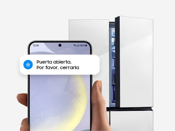 Una mano sostiene un smartphone Galaxy frente a una heladera que muestra la interfaz de usuario de la aplicación SmartThings con la notificación de puerta abierta.