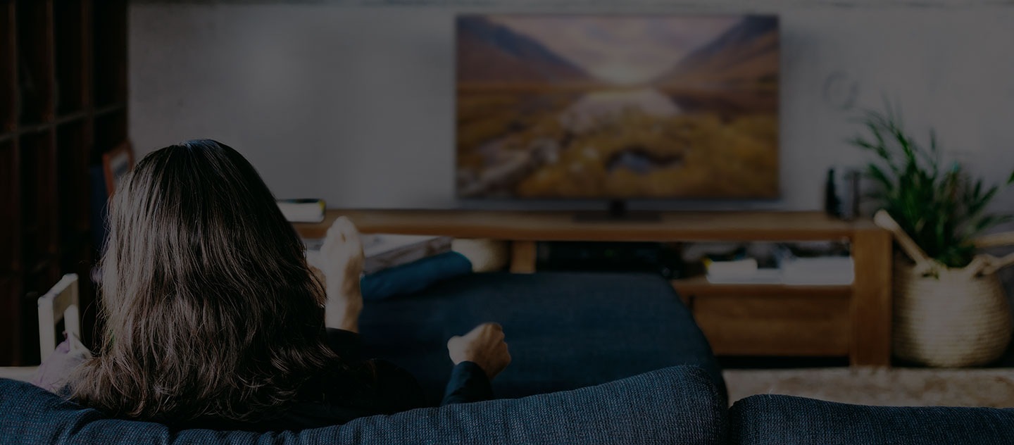 Eine Frau sitzt auf einem Sofa in ihrem Wohnzimmer und sieht fern auf ihrem Wohnzimmer-TV. 
