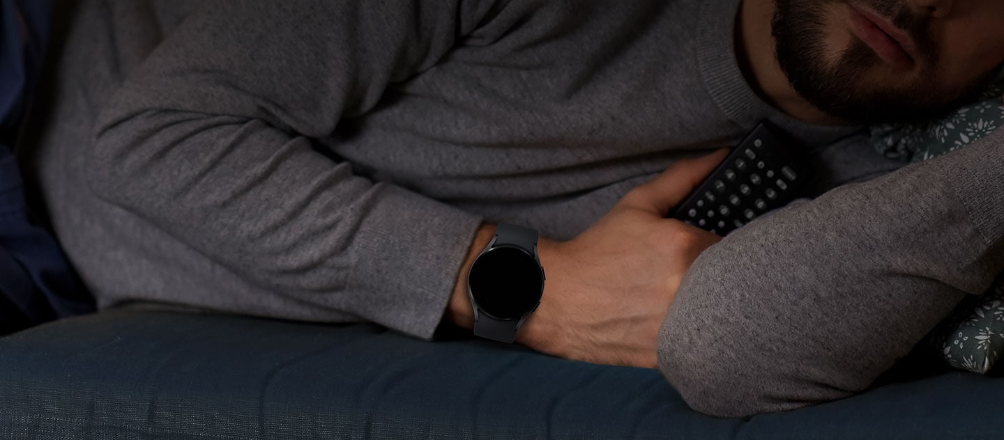 Ein Mann, der eine Galaxy Watch trägt, schläft und hält dabei eine Fernbedienung in der Hand.