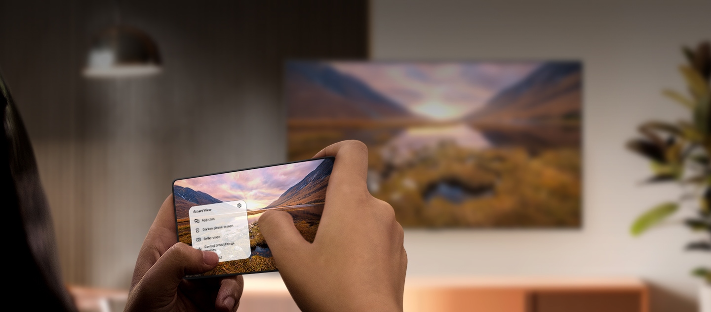 Ein Galaxy Smartphone überträgt ein Bild einer majestätischen Landschaft auf einen Samsung TV im Hintergrund. Der TV zeigt dasselbe Landschaftsbild an.