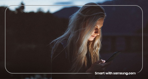 Eine Frau schaut bei Dämmerung auf ihr erleuchtetes Galaxy Smartphone.