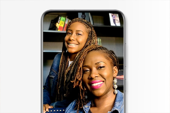 Selfie of a mom and teenage daughter shown on-screen of Galaxy S20, the picture is taken from their home and they are wearing matching jean jackets.