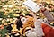 A woman lays down in a lawn full of autumn leaves, dressed in a cozy jacket and scarf, while using her Galaxy Tab S7.