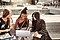 A group of three cheerful female students sitting on a bench in front of a Samsung Galaxy Book2 Pro 360.