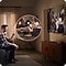 Man wearing a Galaxy Watch watches TV in a living room. He moves his hand back and forth to play the video on the screen with Universal Gestures.