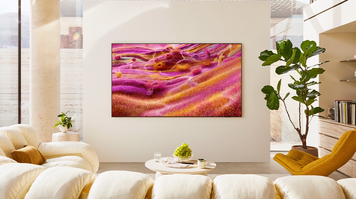 A 98 inch Supersize TV is mounted on a wall in a living room displaying colorful buildings.