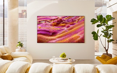 A 98 inch Supersize TV is mounted on a wall in a living room displaying colorful buildings.