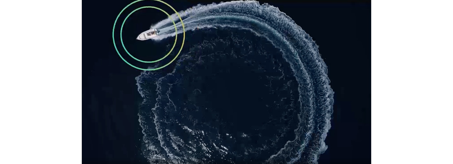 From an overhead wide-shot view of a boat on open water, an animated ripple graphic is superimposed onto the boat to illustrate Object Tracking Sound Plus technology which allows the boat's sound to follow the boat.