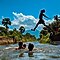 Group of young men swimming in the lake and one man jumping into the water, spreading his arms and legs in the air
