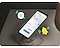 A Samsung Galaxy phone is shown in a close-up, lying face up skewed slightly to the right. The Samsung Galaxy phone is on top of a clear phone stand. There is a yellow bell-shaped alert illustration and the illustration of the SmartThings icon, all showing the different functions old Samsung Galaxy devices can be used as.