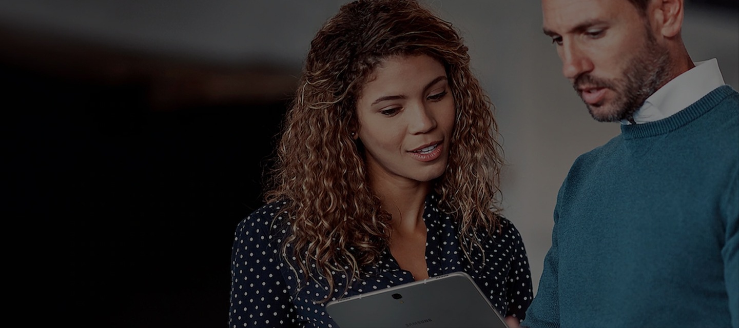 We zien twee medewerkers in gesprek met elkaar terwijl ze naar het scherm van een Galaxy tablet kijken.