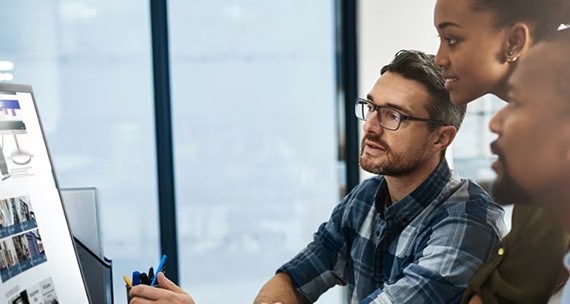 We zien drie collega's die in gesprek met elkaar zijn. Tegelijkertijd kijken ze naar het PC-scherm..