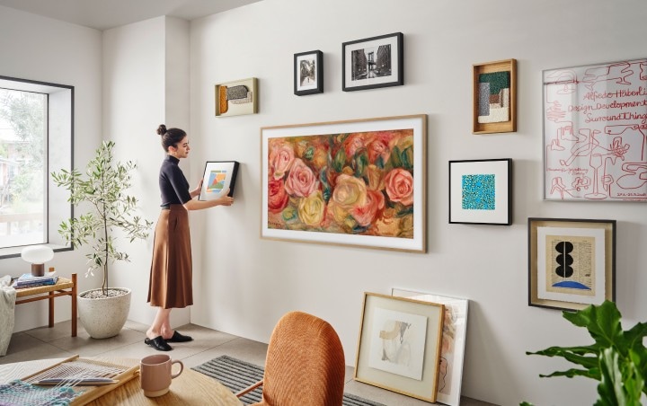 Vrouw hangt de Samsung Music Frame op naast The Frame van Samsung, aan een muur met veel andere kunst.