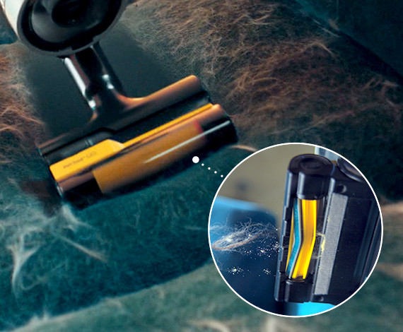 We zien een close-up van een Samsung Jet-stofzuiger met de Pet Tool+-accessoire waarmee huisdierharen van een bank verwijderd worden. De V-vormige trommel en zelfvermalende functies van de Pet Tool+-accessoire zijn gemarkeerd aan de rechterkant.