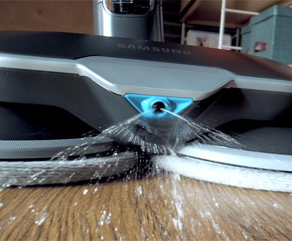 We zien een Samsung Jet-stofzuiger met de spinning sweeper-accessoire en natte dweilen die water op de grond spuit.