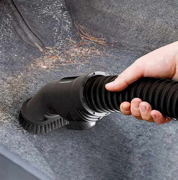 We zien een hand die de Samsung Jet-stofzuiger gebruikt met een verlengde slang en een borstel om vuil van een grijs stoffen oppervlak te verwijderen.