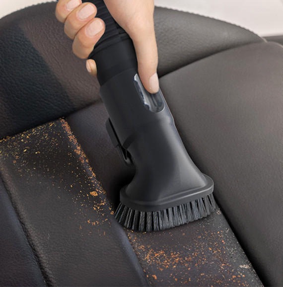 We zien een close-up van een hand die de Samsung Jet-stofzuiger gebruikt met een Hardnekkige Stofborstel om vuil van een leren autostoel te reinigen.