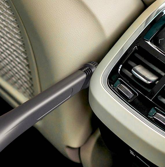 We zien de kierenzuigmond van een Samsung Jet-stofzuiger waarmee de krappe ruimte tussen het dashboard en een stoel van de auto wordt gereinigd.