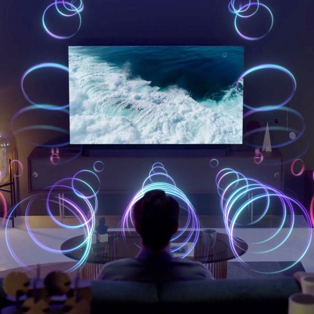 Un homme regarde des images de l'océan sur la télévision dans le salon et écoute le son via la Soundbar. Les ondes sonores sont projetées par les enceintes de la TV orientées vers le haut et via la Soundbar.