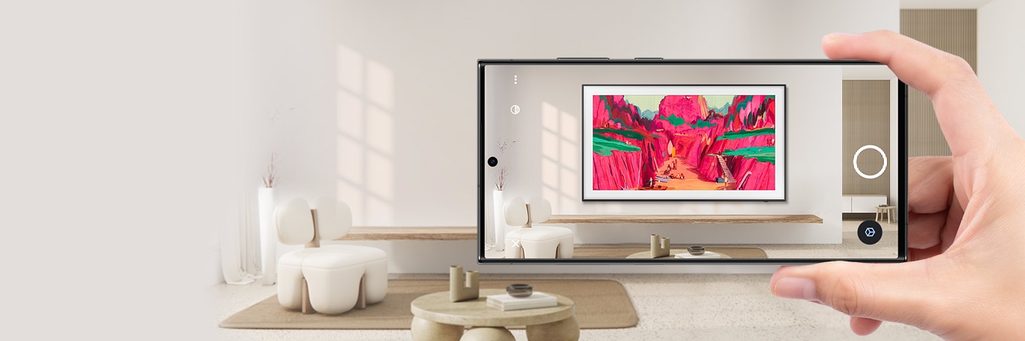 Une main tient un smartphone dans un salon. L'écran du smartphone montre à quoi ressemble The Frame installé sur le mur via RA.