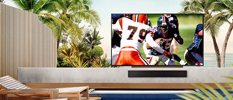 La télévision est installée dans un espace extérieur au bord de la piscine, diffusant un match de football.