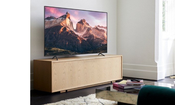 À l'intérieur d'un salon bien éclairé, The Frame TV est placée sur un meuble TV à l'aide de l'option Studio Stand et est vu en gros plan latéral moyen. Une image de montagne avec coucher du soleil est affichée à l'écran.