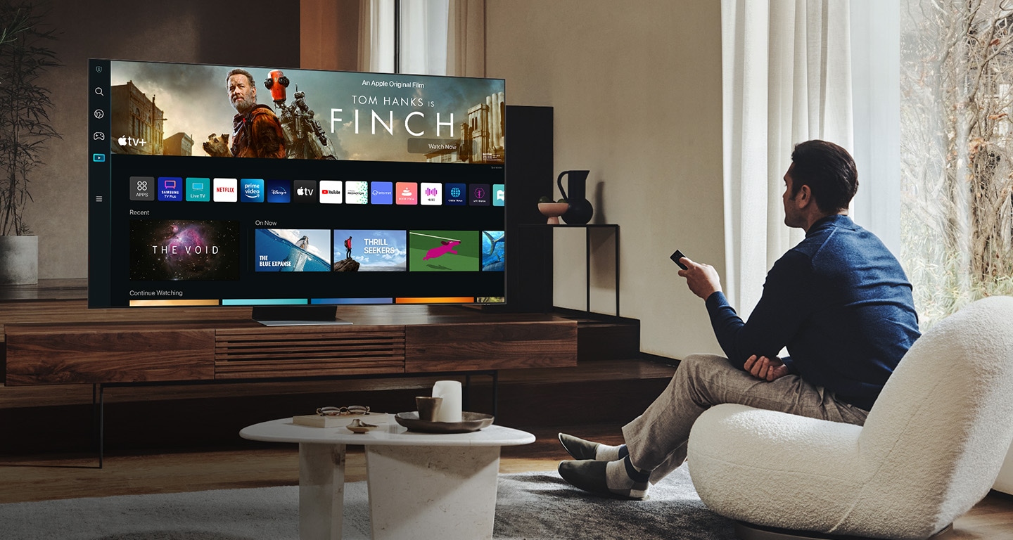 Мъж седи в хола и разглежда новия потребителски интерфейс на Smart Hub на своя телевизор Neo QLED.